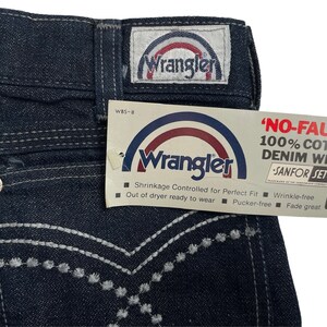 May include: A pair of dark blue denim jeans with white stitching and a Wrangler tag. The tag says "NO-FAULT" 100% COTTON DENIM WITH "SANFOR SET".