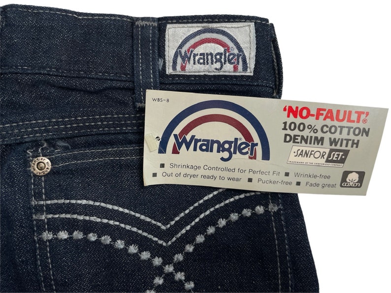 May include: A pair of dark blue denim jeans with white stitching and a Wrangler tag. The tag says "NO-FAULT" 100% COTTON DENIM WITH "SANFOR SET".