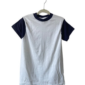 May include: A white t-shirt with navy blue sleeves and a navy blue trim around the neck. The shirt is hanging on a hanger.