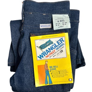May include: A pair of blue denim Wrangler jeans with a tag attached. The tag is yellow and features a cartoon illustration of a person wearing flared jeans. The tag reads "Wrangler 'No-Fault' Denims 100% Cotton 14 oz. Denims with Sanfor-Set Big Bell Jeans".