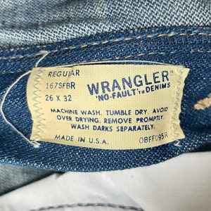 Może przedstawiać: Zbliżenie na niebieską metkę dżinsową z białym tekstem. Na metce widnieje napis "Regular 167SFBR 26 X 32 Wrangler 'No-Fault' Denim Machine Wash. Tumble Dry. Avoid Over Drying. Remove Promptly. Wash Darks Separately. Made in U.S.A. OBFFD95R"