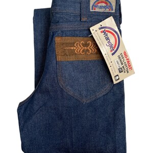 May include: A pair of blue denim jeans with a brown corduroy patch on the back pocket. The jeans have a Wrangler label on the back waistband and a tag that reads "No-Fault 100% Cotton Denim with Sanforized".