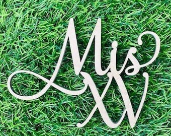 May include: White wooden cutout of the word "Miss" with a decorative swirl and the number "XV" in a cursive font.