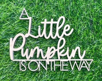 May include: A white wooden sign with the text "A little pumpkin is on the way" in a cursive font.
