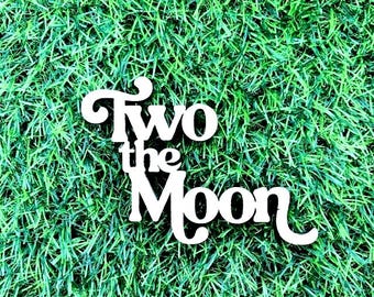 May include: White wooden sign with the text "Two the Moon" on a green grass background.