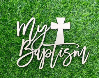 May include: Wooden sign with the text "My Baptism" in a cursive font. A wooden cross is centered above the text.