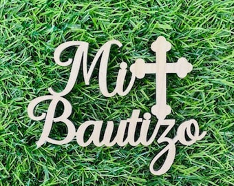 May include: Wooden sign with the words "Mi Bautizo" and a cross in a cursive font. The sign is on a green grass background.