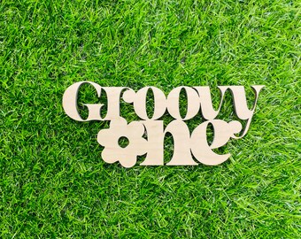 May include: Wooden sign with the text "Groovy One" in a retro font. The sign has a small flower cutout in the center.