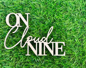 May include: Wooden sign with the text "On Cloud Nine" in white letters on a green grass background.