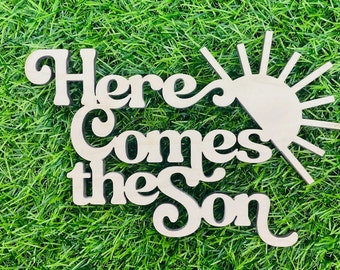 May include: Wooden sign with the text "Here Comes the Sun" in a retro font. The sun is depicted with rays emanating from it.