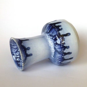 Könnte beinhalten: Eine weiße Keramikvase mit blau-weißem Überzug. Die Vase hat eine breite Öffnung und einen schmalen Hals. Der Überzug hat einen Tropfeffekt, der einen einzigartigen und künstlerischen Look erzeugt.