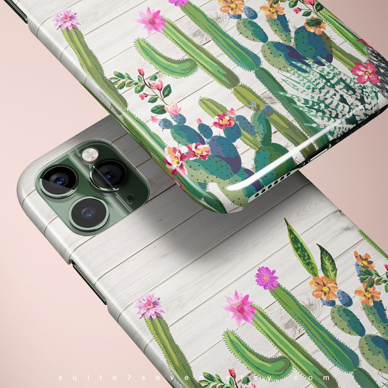 May include: A white phone case with a wood grain pattern and a cactus and flower design. The phone case is shown with a green phone with a camera lens.
