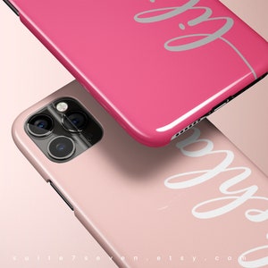 May include: Two pink phone cases with a white cursive design that says "Pretty". The phone cases are stacked on top of each other.