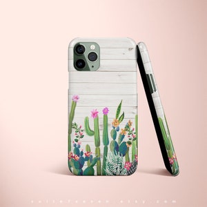May include: A white phone case with a wood grain pattern and a green cactus design. The case has a cutout for the camera lens.