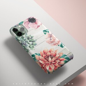 Pu&ograve; includere: Una custodia per telefono bianca con un design floreale. La custodia presenta fiori rosa, rossi e verdi su uno sfondo in legno bianco.