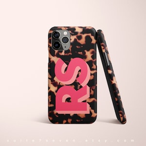May include: A black and brown tortoiseshell patterned phone case with the letters "RS" in pink and orange. The case is designed for an iPhone.