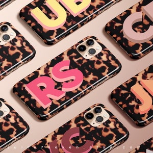 May include: A collection of iPhone cases with a tortoiseshell pattern and large, colourful, 3D letters. The letters are in various colours, including pink, orange, yellow, and grey.