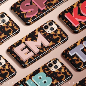 May include: A set of ten phone cases with a tortoiseshell pattern and large, colourful letters. The letters spell out the words "SP", "KG", "EM", "TL", "UB".