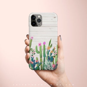 May include: A white iPhone case with a woodgrain background and a cactus and flower design. The case has a camera cutout and a white border.
