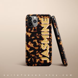May include: A brown and black tortoiseshell iPhone case with a gold "JASMINE" name printed on the back.
