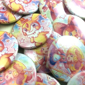 May include: A collection of colorful round buttons featuring a cartoon character with a halo and wings. The character is depicted in a variety of poses and settings, including a pink and blue background with stars.