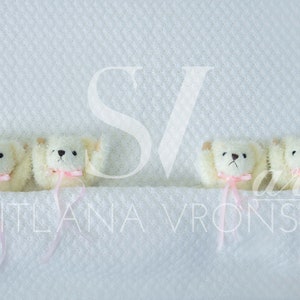 May include: Four white teddy bears with pink bows are lined up on a white textured surface. The bears are facing forward with their arms raised.