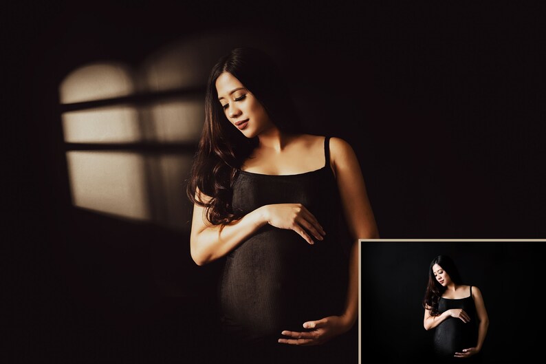 Peut inclure: Une femme enceinte portant un d&eacute;bardeur noir se tient dans une pi&egrave;ce faiblement &eacute;clair&eacute;e avec une fen&ecirc;tre derri&egrave;re elle. La lumi&egrave;re de la fen&ecirc;tre projette une ombre sur le mur derri&egrave;re elle. Elle se tient le ventre avec les deux mains.