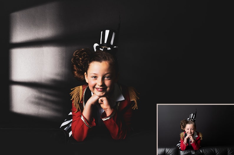 Peut inclure: Une jeune personne portant un costume de ma&icirc;tre de c&eacute;r&eacute;monie rouge et noir avec un chapeau haut de forme noir et blanc. Elle est assise sur une surface noire et sourit &agrave; la cam&eacute;ra.