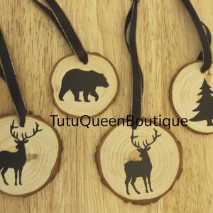 May include: Four rustic wooden ornaments featuring black silhouettes of a bear, a pine tree, and two deer. Each is a wood slice with a dark ribbon. The text "TutuQueenBoutique" is visible on the wood. Ideal for Christmas.