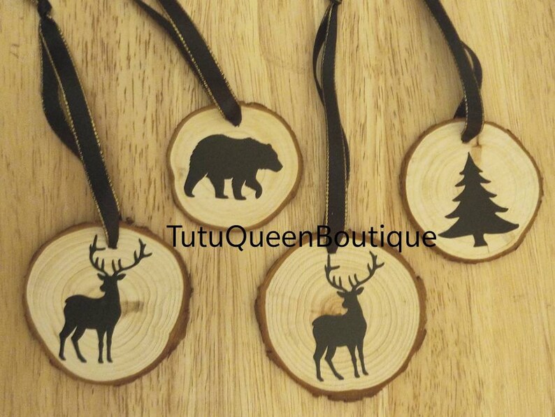 May include: Four rustic wooden ornaments featuring black silhouettes of a bear, a pine tree, and two deer. Each is a wood slice with a dark ribbon. The text "TutuQueenBoutique" is visible on the wood. Ideal for Christmas.