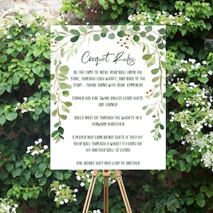 May include: A white sign with green foliage border and the text "Croquet Rules" with instructions for playing the game. The sign is on a wooden easel.