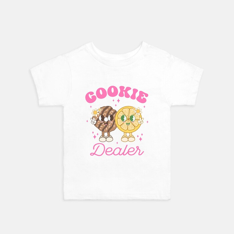 May include: White t-shirt with a pink graphic of a cookie and a lemon slice with the text "COOKIE DEALER".