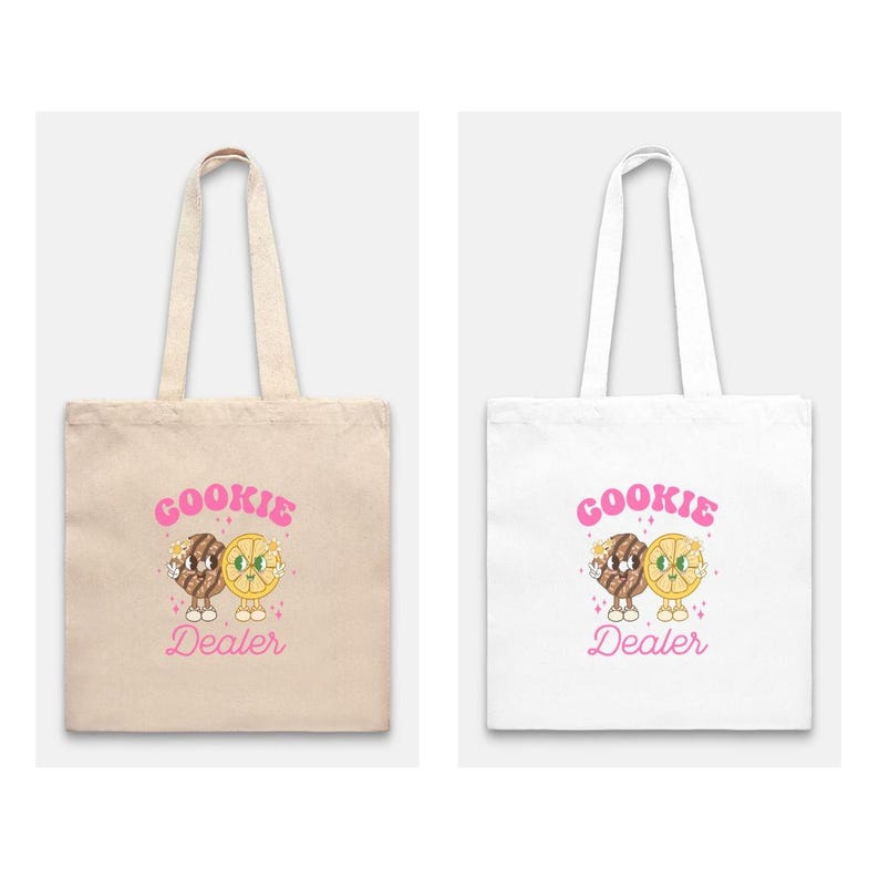 May include: Two tote bags with a cartoon cookie and lemon design. The text "COOKIE DEALER" is printed in pink on both bags. One bag is beige and the other is white.