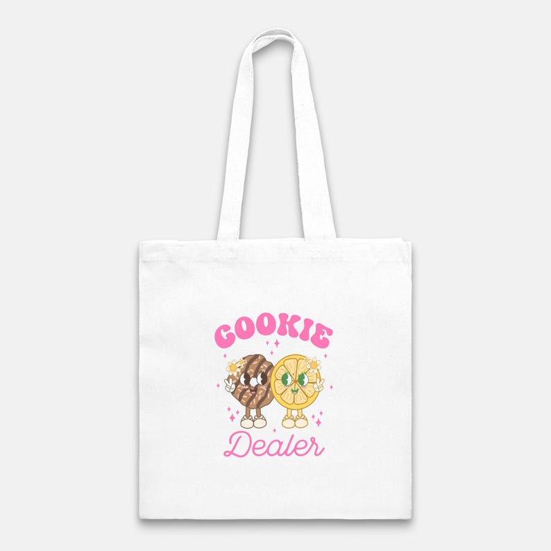 May include: White tote bag with a pink graphic of a cookie and a lemon slice with the text "COOKIE DEALER".