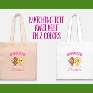 May include: Two tote bags with pink text that reads "COOKIE DEALER" and a cartoon image of a cookie and a lemon slice. The tote bags are available in two colors: natural and white.