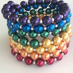 Peut inclure: Un ensemble de six bracelets en perles arc-en-ciel. Les bracelets sont faits de perles irisées dans les tons de violet, bleu, vert, jaune, orange et rouge.