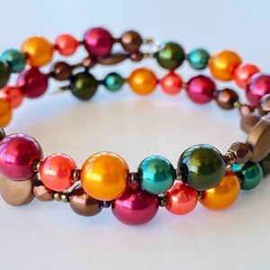 May include: A multi-strand bracelet with a mix of round and oval beads in shades of red, orange, yellow, green, and brown.