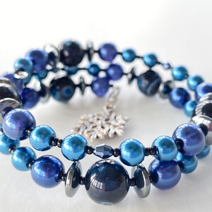 May include: A blue and silver beaded bracelet with a snowflake charm. The bracelet is made with various shades of blue beads, including dark blue, light blue, and silver.
