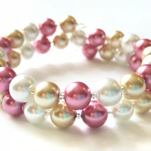 May include: A double-strand bracelet made with white, pink, and gold pearls. The bracelet is made with a wire and has a simple design.