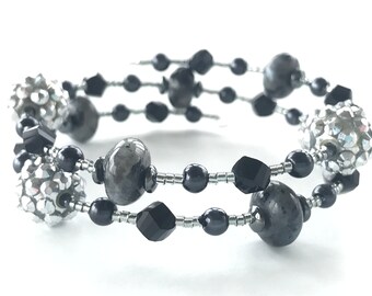 May include: A double-strand bracelet featuring black and silver beads. The bracelet includes round, faceted black beads, round silver beads, and larger, round, grey beads.