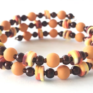 Könnte beinhalten: Ein mehrreihiges Armband mit braunen, orangefarbenen und gelben Perlen. Die Perlen sind in einem sich wiederholenden Muster angeordnet.