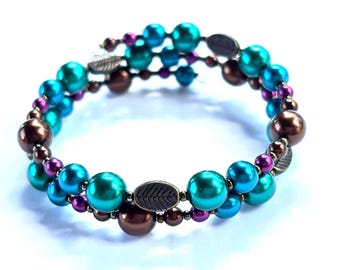 May include: A spiral bracelet with teal, blue, brown, and purple beads. The bracelet features a mix of large and small beads, with metal leaf accents. The beads are arranged in a spiral pattern, creating a unique piece of jewellery.