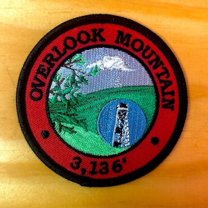 May include: A red and black embroidered patch with the text "Overlook Mountain 3,136'" and a depiction of a mountain with a tower on top.