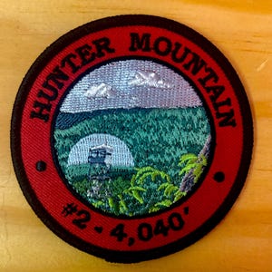 May include: Red embroidered patch with black trim, depicting a mountain scene with a lookout tower. The text "Hunter Mountain #2 - 4,040'" is embroidered in black.