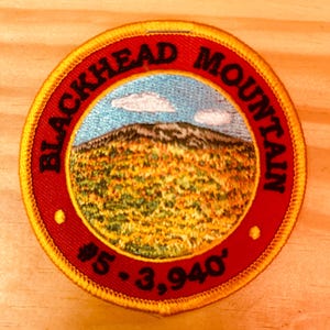 May include: A red and gold embroidered patch with the text "Blackhead Mountain #5 - 3,940'" and a depiction of a mountain with a blue sky and white clouds.
