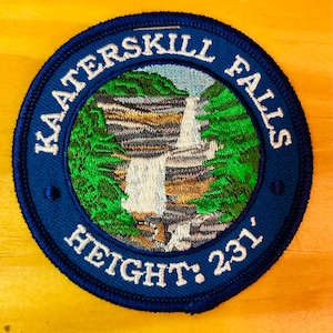 May include: A blue embroidered patch with the text "Kaaterskill Falls Height: 231'" and a depiction of a waterfall in a green forest.