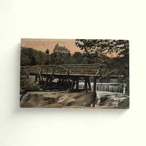 May include: A vintage postcard depicting a wooden bridge over a waterfall, with a large house in the background. The text on the postcard reads " Haines Falls Bridge and Riley Cottage, Catskill Mountains, N.Y."
