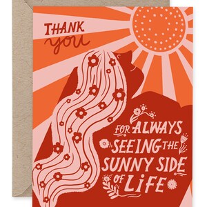 May include: A greeting card in shades of orange, red, and pink. The card reads "Thank You" and "For Always Seeing the Sunny Side of Life." The design includes a stylized illustration of a person's hair with flowers and a sun.