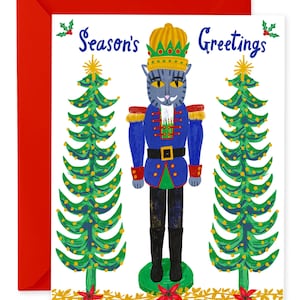 Op de afbeelding: Een feestelijke wenskaart met een rode envelop. De kaart toont een blauwe kat verkleed als notenkraker, met een gouden kroon, en de woorden "Season's Greetings". Twee groene kerstbomen flankeren de kat, met rode poinsettia's onderaan.