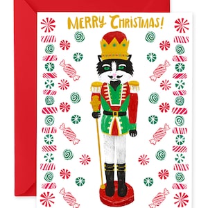May include: A Christmas card with a red envelope. The card features a cat dressed as a nutcracker with the words "MERRY CHRISTMAS!" in gold. The card is decorated with candy cane and snowflake designs.